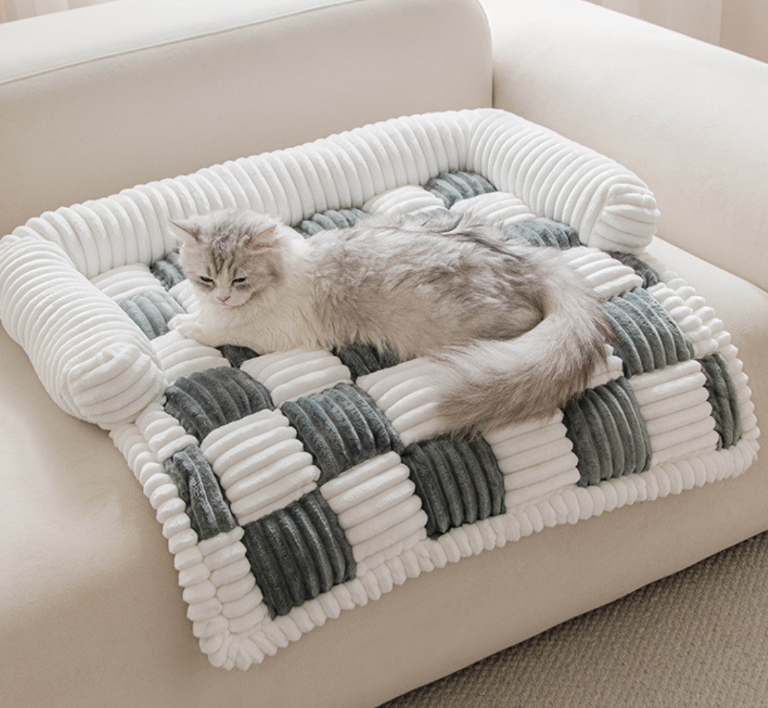 Fluffy Fuzzy Calming Dog Bed Sofa Protector Pet Mat Cat lying on a checkered pet bed with white and gray colors on a beige sofa.